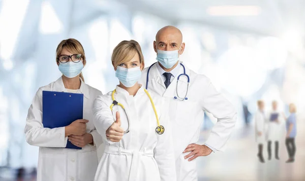 顔のマスクを着用した医療チームのショットと一緒に病院のホワイエに立っている間 女性医師は親指を放棄 — ストック写真