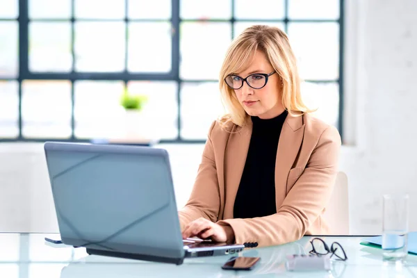 迷人的女商人头戴眼镜 工作时使用笔记本电脑 微笑着坐在办公室里工作的女性 — 图库照片