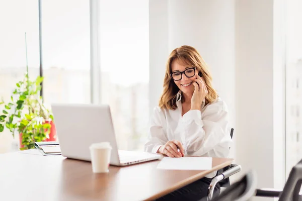 一名中年职业女性穿着衬衫 在一间现代化的办公室工作时使用笔记本电脑 坎迪拍摄的照片 迷人的女商人坐在办公桌前 有一个商务电话 — 图库照片