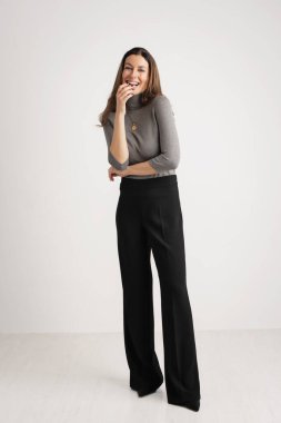 Çekici, dişlek, gülümseyen ve kameraya bakan bir kadın. Esmer, kadın balıkçı yaka kazak ve pantolon giyerken izole beyaz arka planda duruyor. Boşluğu kopyala. 