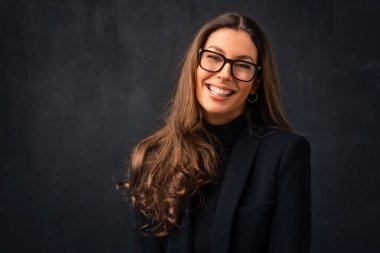 Kapalı arka planda poz verirken boğazlı kazak ve gözlük giyen, dişlek gülüşlü, çekici, orta yaşlı bir kadının yakın çekimi. Uzayı kopyala Stüdyo çekimi. 