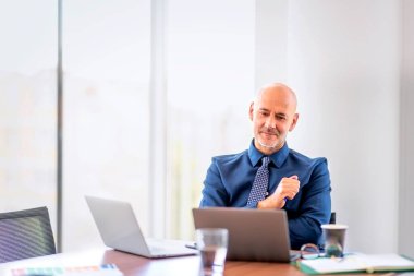Orta yaşlı işadamının modern bir ofiste oturup dizüstü bilgisayar kullanırken çekilmesi. Profesyonel erkek gömlekli ve kravatlı.. 