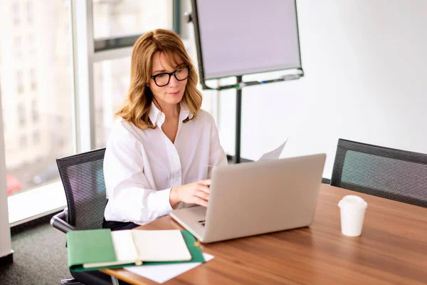 在现代化的办公室工作时 中年职业女性穿着衬衫 使用笔记本电脑 头戴眼镜的金发女商人 — 图库照片