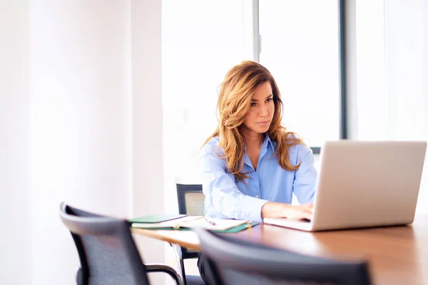 在现代化的办公室工作时 中年妇女穿着衬衫 使用笔记本电脑 — 图库照片
