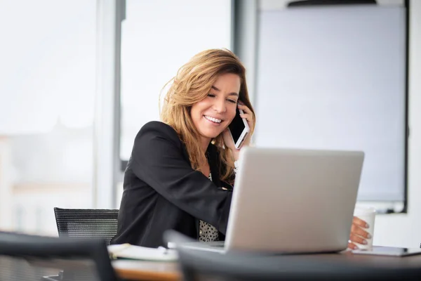 在现代化的办公室工作的中年职业女性 有一个商业电话和使用笔记本电脑 职业女性穿着夹克 — 图库照片