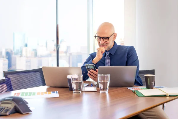 Zdjęcia Biznesmena Średnim Wieku Siedzącego Nowoczesnym Biurze Używającego Smartfona Laptopów — Zdjęcie stockowe