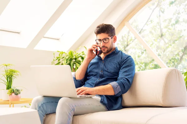 在家工作时用智能手机和笔记本电脑思考的男人 自信的男人坐在沙发上打电话 总部办公室 — 图库照片
