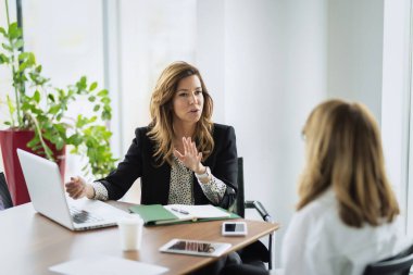 Bir grup iş kadını masa başında dizüstü bilgisayar kullanıyor ve iş görüşmesinde fikrini sunuyor. Modern bir ofiste takım çalışması..