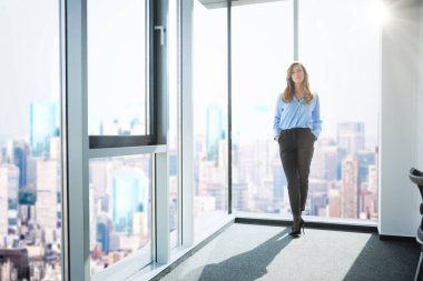 Kollarını kavuşturup pencerenin önünde dikilirken düşünceli bir şekilde bakan çekici bir kadın..