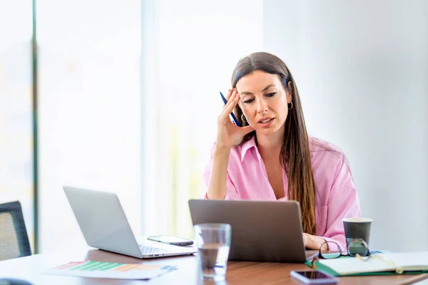 中年女商人坐在办公室里 若有所思地看着 工作时使用手提电脑时自信的专业女性 — 图库照片