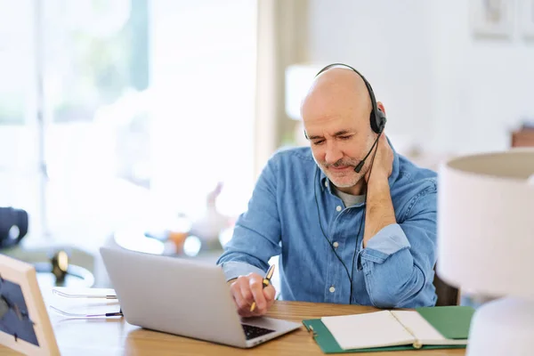 stock image Customer service assistant wearing headset while sitting behind his laptop and working in the call center. Handsome businessman wearing denim shirt. 