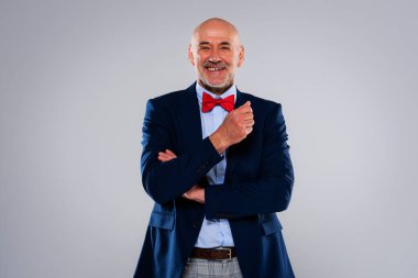 İzole edilmiş gri arka planda dururken komik suratlı adamın stüdyo fotoğrafı pantolonunu ve papyonunu kontrol etti. Boşluğu kopyala.