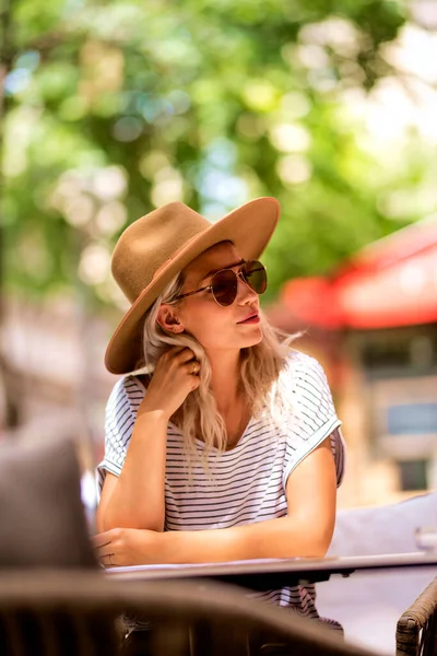 Стильная Женщина Повседневной Одежде Современной Шляпе Солнцезащитных Очках Сидящая Столом — стоковое фото