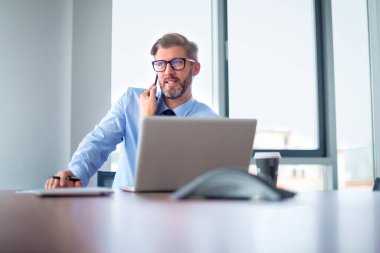 Orta yaşlı işadamı ofis masasında oturuyor ve iş görüşmesi yapıyor. Not defteri kullanan kendine güvenen profesyonel bir adam..