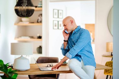 Bilgisayarı kullanan ve masa başında çalışırken telefonla konuşan bir adamın görüntüsü.. 