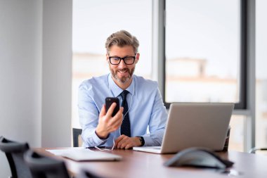 Orta yaşlı iş adamı ofiste oturuyor ve çalışıyor. Profesyonel bir adam kulaklık kullanıyor ve video görüşmesi yapıyor.. 