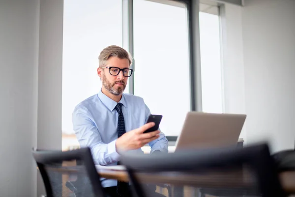 深刻な顔のビジネスマンは オフィスに座って 仕事のために携帯電話やラップトップを使用しています プロの男性テキストメッセージ — ストック写真