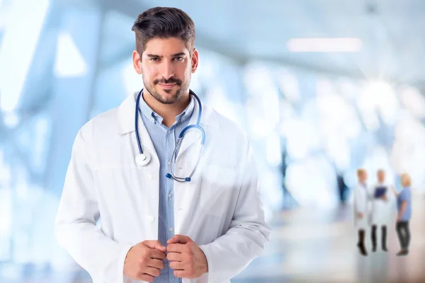 自信的医学专业人员的形象 笑着的成熟男医生穿着实验室的外套 他站在诊所里 3位同事站在后台 — 图库照片