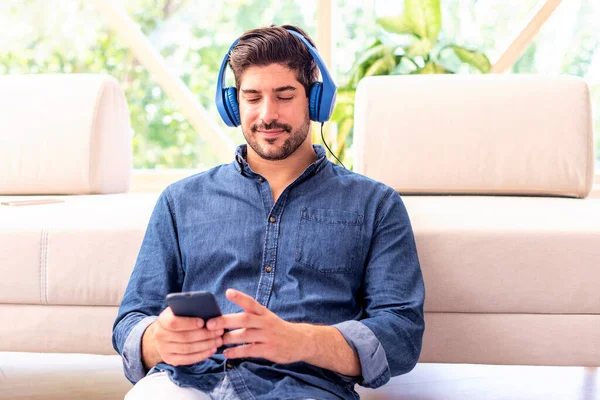 Hombre Está Sentado Sofá Casa Con Auriculares Teléfono Móvil Escuchando —  Fotos de Stock