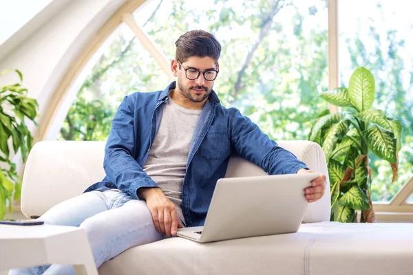 一个英俊的男人 他坐在沙发上 用笔记本电脑工作 有视频通话的白人男性 — 图库照片