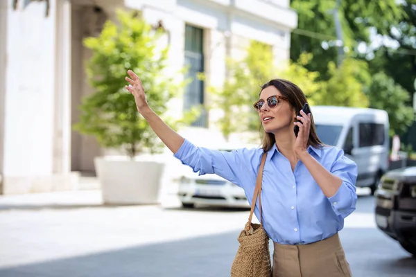 Привлекательная Женщина Поднимает Руку Вызвать Такси Идя Улице Имея Телефонный — стоковое фото