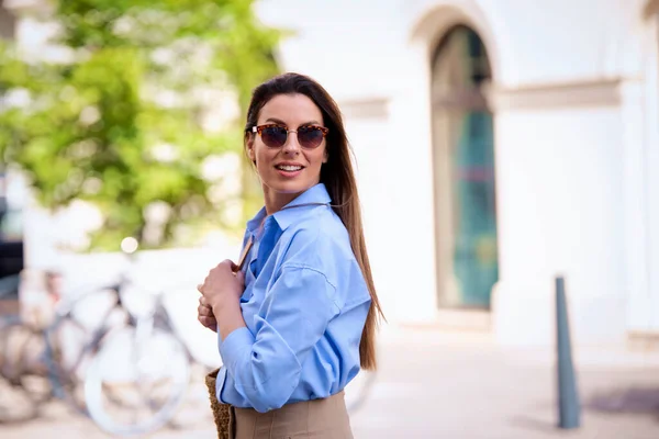 快乐的黑发女人 戴着太阳镜 穿着蓝色衬衫 走在城里的大街上 — 图库照片