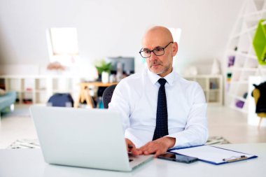 Ofis masasında oturan orta yaşlı bir işadamı ve iş için dizüstü bilgisayar kullanıyor. Yönetici erkek gömlek ve kravat takıyor ve mali beyanname üzerinde çalışıyor.. 