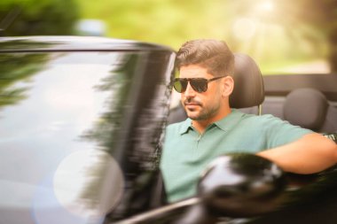 Güneş gözlüğü takan, üstü açık bir arabada oturan ve yolda araba süren yakışıklı bir adam.. 
