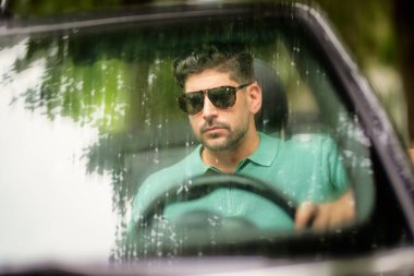 Güneş gözlüğü takan, üstü açık bir arabada oturan ve yolda araba süren yakışıklı bir adam.. 