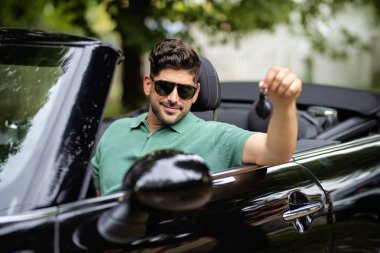 Üstü açık arabada oturan ve elinde araba anahtarı tutan yakışıklı bir adam.. 