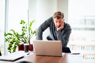 Orta yaşlı bir işadamının modern bir ofiste dizüstü bilgisayarı iş için kullandığını düşünmek. Profesyonel erkek düşünceli görünüyor ve video konferansı yapıyor.. 