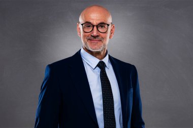 Koyu gri arka planda duran orta yaşlı bir iş adamının portresi. Takım elbiseli ve gözlüklü kendine güvenen profesyonel bir adam. Boşluğu kopyala.