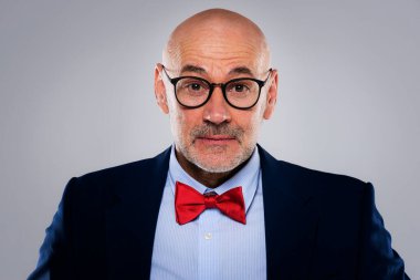 Gri bir arkaplanda duran orta yaşlı bir iş adamının vesikalığı. Takım elbiseli, papyonlu, özgüvenli ve düşünceli bir adam. Boşluğu kopyala.