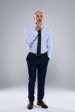 Gri arka planda sorunlu duran orta yaşlı bir iş adamı. Stüdyo çekimi. İş gömleği ve kravat takan kendinden emin bir erkek. Uzayı kopyala Tam boy çekim. 