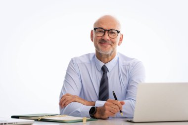 Orta yaşlı işadamı masasında oturuyor ve not defterini izole edilmiş arka plana karşı kullanıyor. Gömlek ve kravat takan kendine güvenen profesyonel bir adam. Boşluğu kopyala.