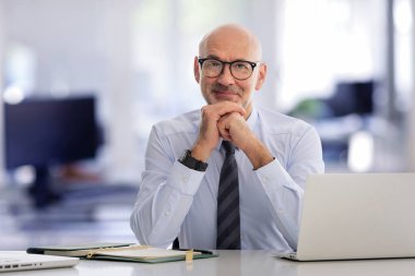 Ofiste oturan orta yaşlı bir işadamı ve not defterini iş için kullanıyor. Gömlek ve kravat takan kendinden emin profesyonel bir adam.. 