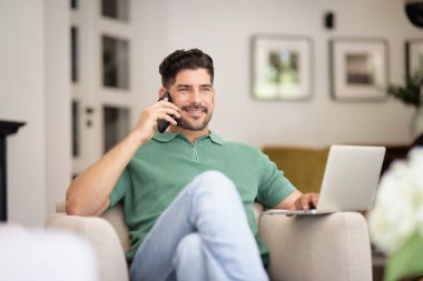 Evde oturup dizüstü bilgisayar ve akıllı telefon kullanan orta yaşlı bir adam. Kendine güvenen bir erkek arama yapıyor. Merkez Ofis.