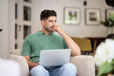 Orta yaşlı bir adam evdeki koltuğunda oturuyor ve iş için dizüstü bilgisayar kullanıyor. Derin düşüncelere dalmış kendinden emin bir iş adamı. Merkez Ofis.