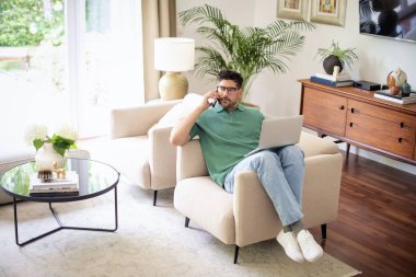 Evde oturup dizüstü bilgisayar ve akıllı telefon kullanan orta yaşlı bir adam. Kendine güvenen bir erkek arama yapıyor. Merkez Ofis.