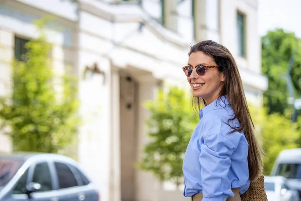 快乐的黑发女人 戴着太阳镜 穿着蓝色衬衫 走在城里的大街上 — 图库照片