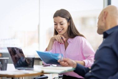 Bir grup iş kadını ve bir iş adamı modern bir ofiste iş toplantısındalar. Masada dizüstü bilgisayarlar ve belgeler var. Takım çalışması..