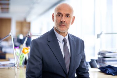 Orta yaşlı bir iş adamının yakın çekimi ofisinde oturuyor ve düşünceli görünüyor. Takım elbiseli ve kravatlı kendine güvenen profesyonel bir adam.. 