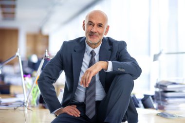 Orta yaşlı bir işadamı ofisinde oturuyor. Takım elbiseli ve kravatlı kendine güvenen profesyonel bir adam.. 