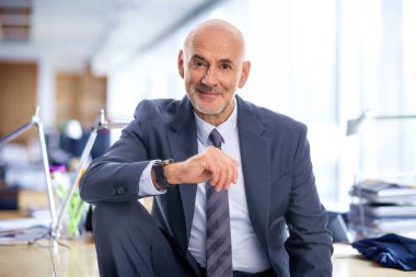 Orta yaşlı bir işadamı ofisinde oturuyor. Takım elbiseli ve kravatlı kendine güvenen profesyonel bir adam.. 