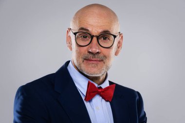 Gri arka planda dikilirken takım elbise ve papyon takan gülümseyen iş adamının görüntüsü. Boşluğu kopyala.