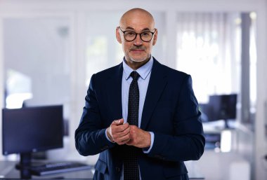 Ofiste duran orta yaşlı bir iş adamının portresi. Takım elbiseli ve kravatlı profesyonel bir adam..