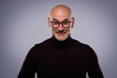 Gri arka planda dikilirken sıradan kıyafetler giyen orta yaşlı yakışıklı bir adamın stüdyo portresi..