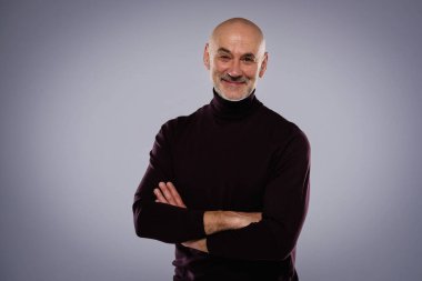 Gri arka planda dikilirken sıradan kıyafetler giyen orta yaşlı yakışıklı bir adamın stüdyo portresi..