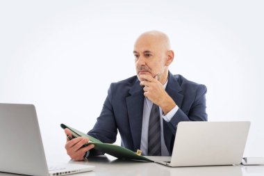 Orta yaşlı işadamı masasında oturuyor ve not defterini izole edilmiş arka plana karşı kullanıyor. Kendine güvenen, takım elbiseli, kravatlı ve defterine özenle bakan profesyonel bir adam..  