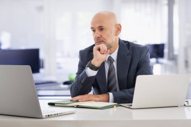 Ofisindeki masasında oturmuş dizüstü bilgisayar kullanan orta yaşlı bir iş adamı. Laptoplara düşünceli bir şekilde bakıyor. Profesyonel yönetici video konferansı yapıyor.. 